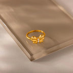 The gold Bow Pearl Ring displayed on a reflective beige surface, showing its polished bow and pearl details.