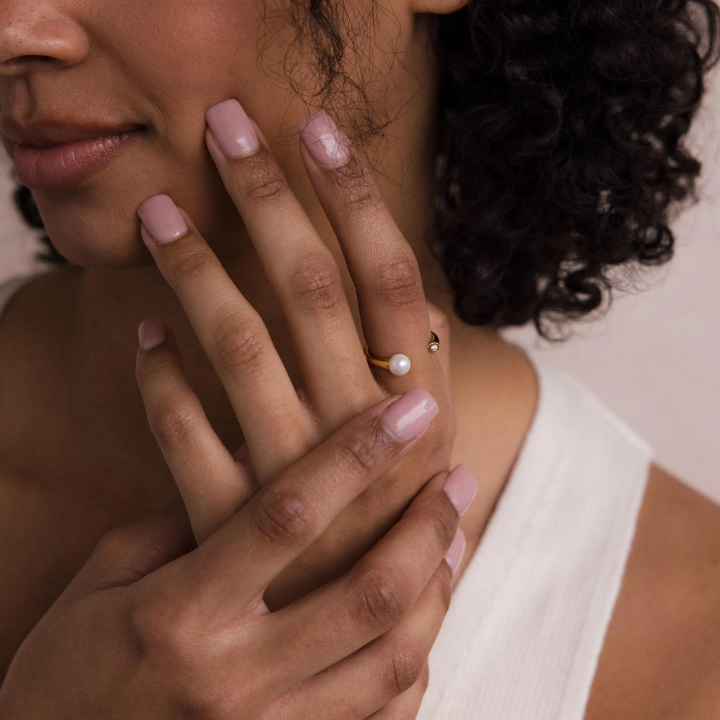 A woman with pink nails touches her face while wearing the elegant Open Pearl & Diamond Ring on her finger.