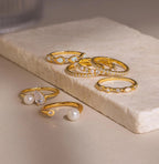 The Open Pearl & Diamond Ring, featuring pearls and diamonds, is displayed elegantly on a rectangular stone slab.
