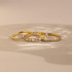 The Diamond Eternity Ring Set, featuring three gold rings, is displayed on a beige surface with soft lighting.