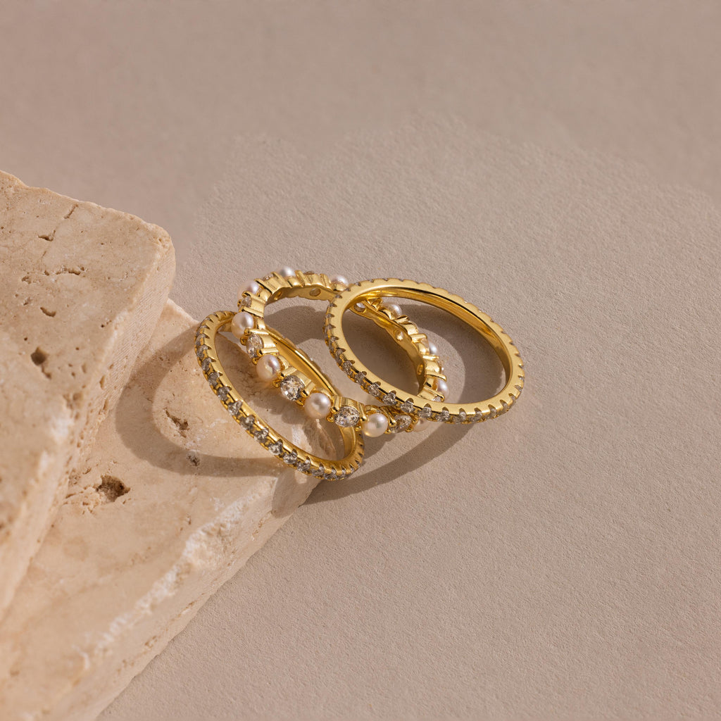 The Diamond Eternity Ring Set, featuring delicate crystal accents and elegant bands, rests on a beige stone surface.