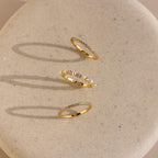 The Diamond Eternity Ring Set, featuring two gold diamond bands and a pearl ring, is elegantly displayed on a beige speckled surface.