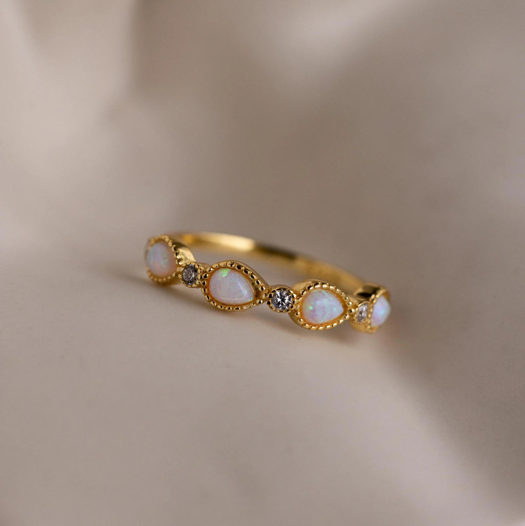 The Opal Diamond Teardrop Ring, featuring shimmering opal and diamond stones, rests on soft beige fabric, exuding timeless elegance.