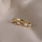 The Opal Diamond Teardrop Ring, featuring shimmering opal and diamond stones, rests on soft beige fabric, exuding timeless elegance.
