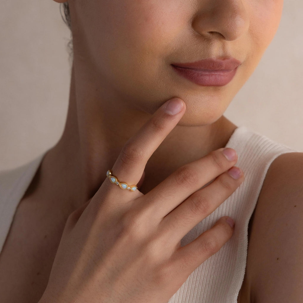 Woman touching her face, wearing the Opal Diamond Teardrop Ring, styled with a sleeveless white top.