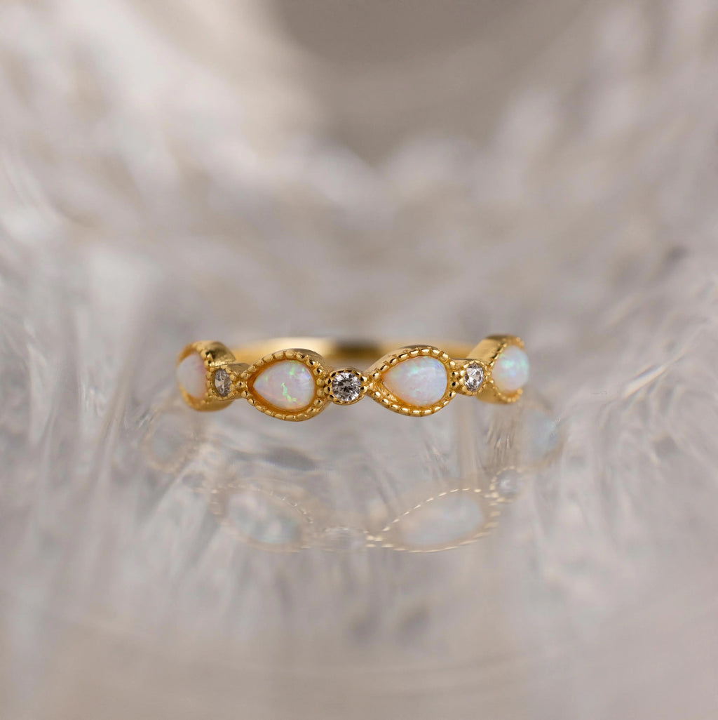 Opal Diamond Teardrop Ring featuring alternating opal and diamond stones, set in an elegant vintage-inspired design with Art Deco influences, showcased against a softly blurred, textured background.