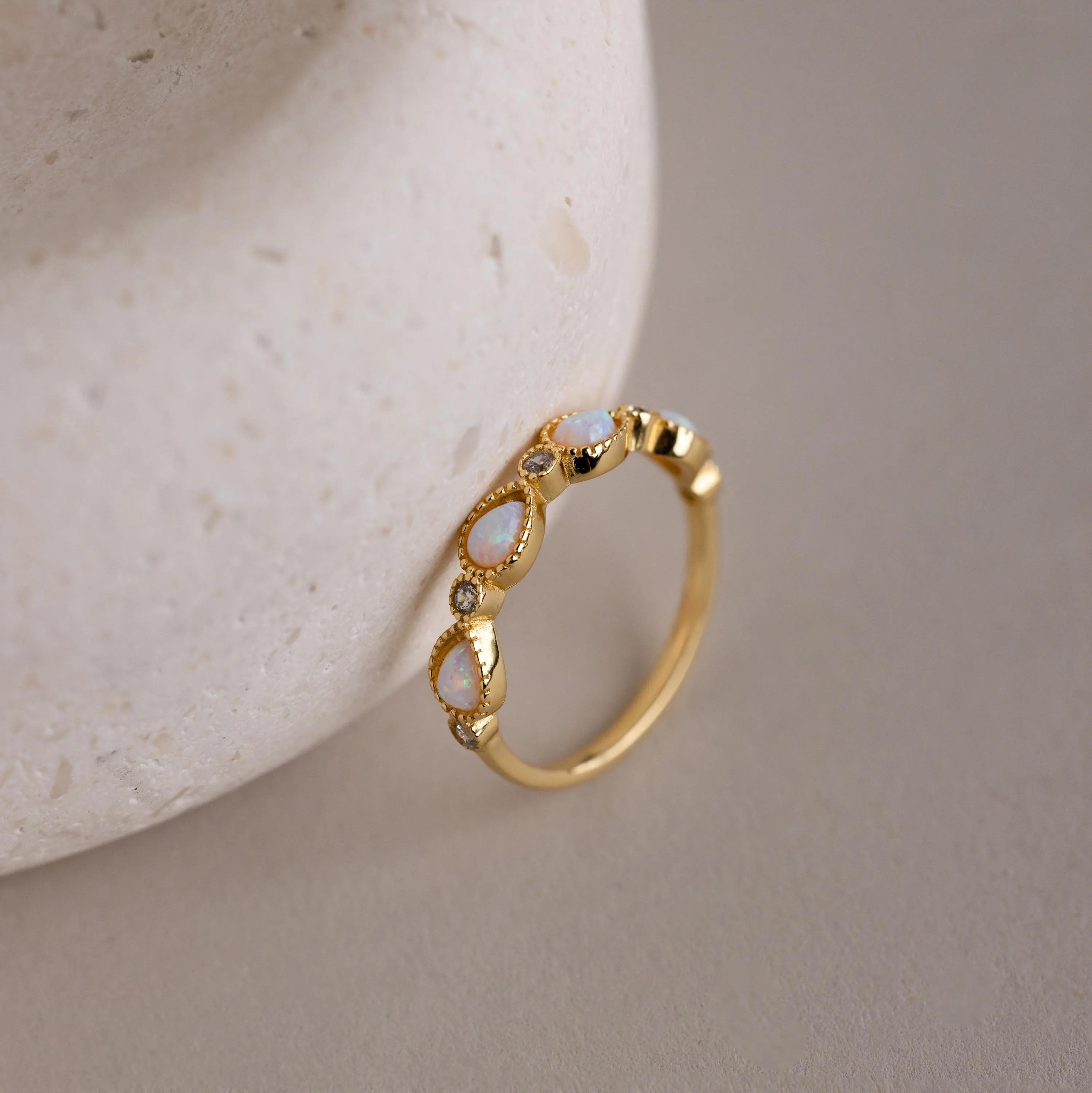 The Opal Diamond Teardrop Ring features teardrop-shaped opal stones set against a textured, light surface, evoking the charm of a vintage-inspired ring.