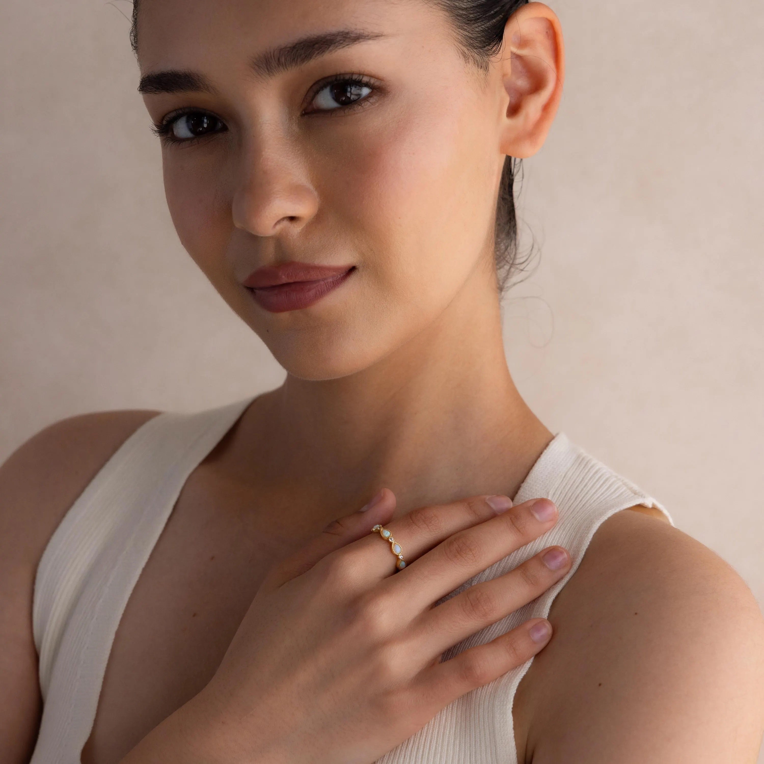 Woman with dark hair in a white top, hand on chest, wearing the Opal Diamond Teardrop Ring, looking at the camera.