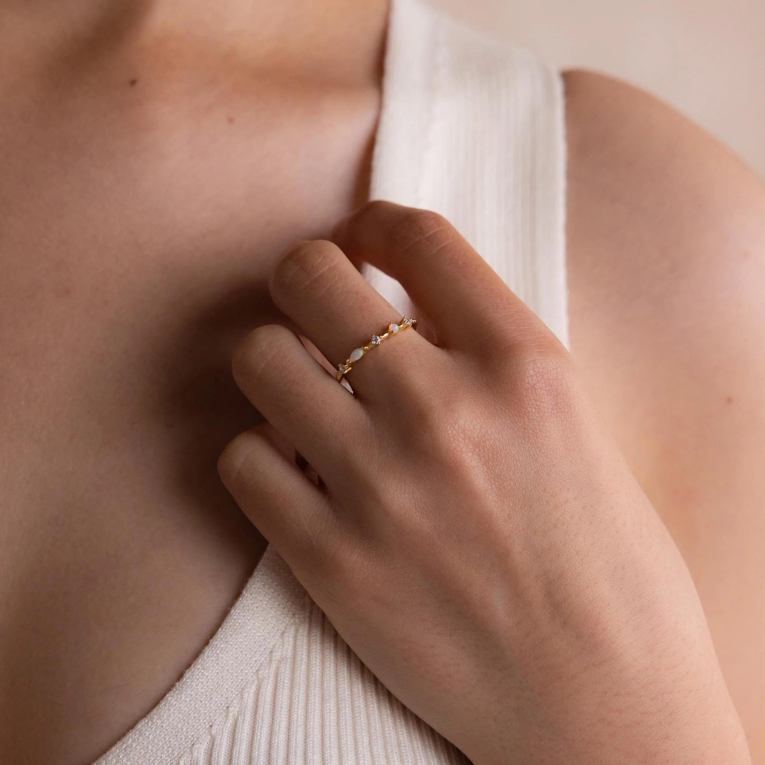 A hand adorned with the Mixed Opal & Diamond Ring rests gently on the collar of a white ribbed sleeveless top.