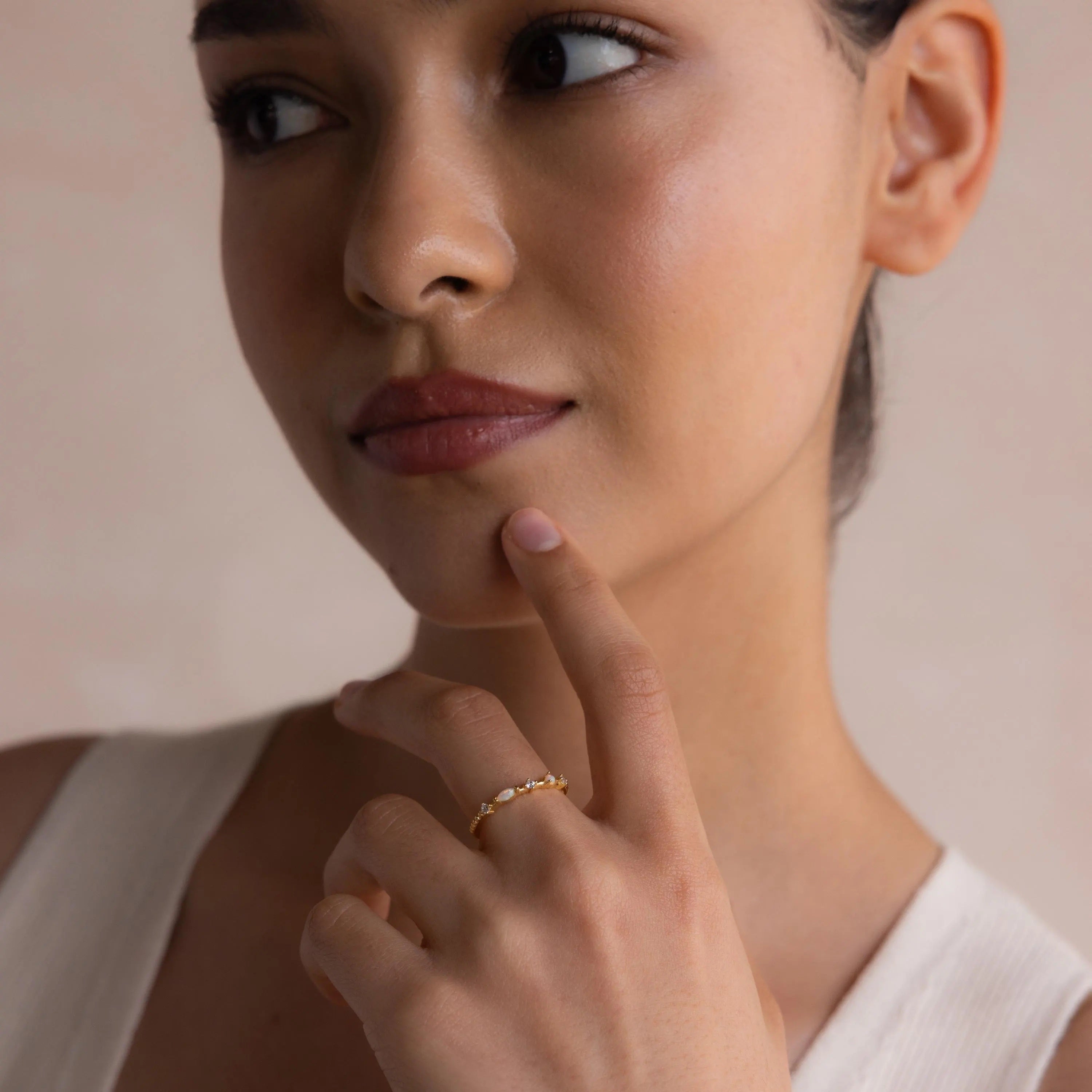 A woman thoughtfully touches her chin, looking slightly to the side while wearing a Mixed Opal & Diamond Ring on her finger.