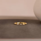 The Mixed Opal & Diamond Ring, a gold band set with opals and diamonds, is displayed on a textured gray surface against a softly blurred background.