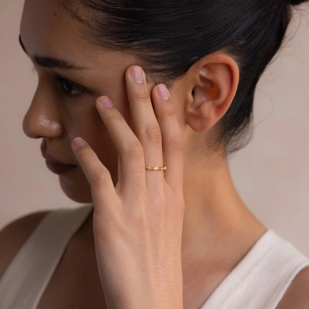 A woman with dark hair touches her face, highlighting the Mixed Opal & Diamond Ring on a gold band under soft lighting.