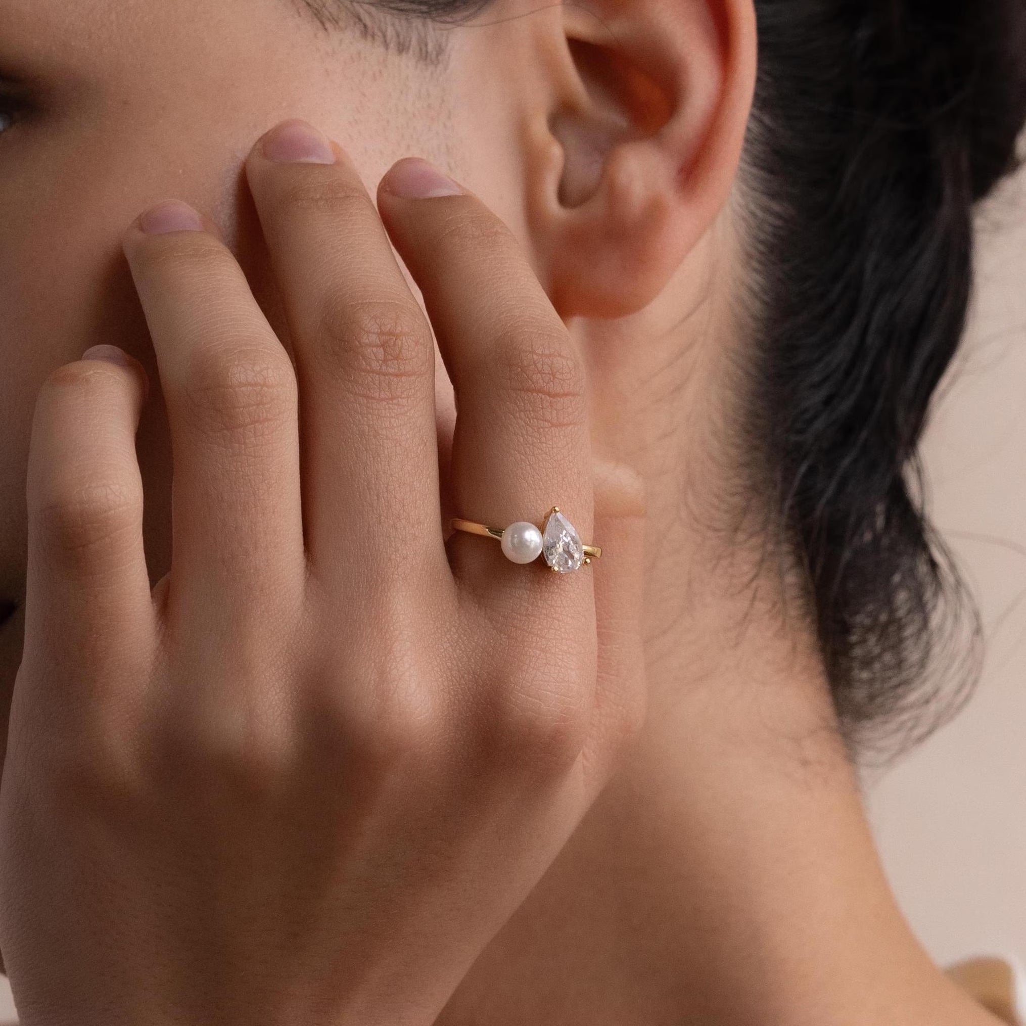 A close-up of a hand wearing the Pearl Diamond Ring, featuring a round pearl and a teardrop-cut diamond set on a slim gold band.