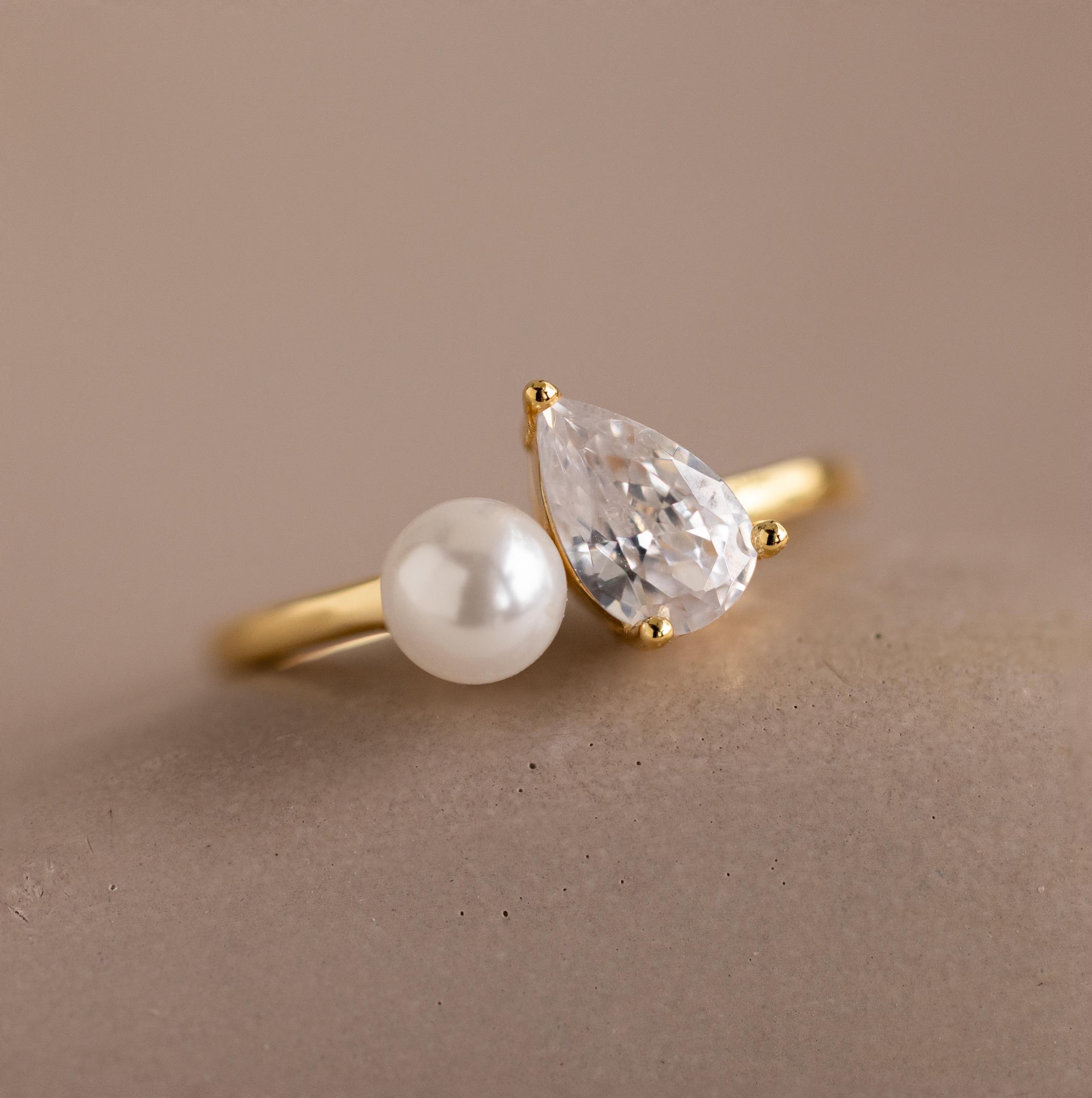 Detailed product shot of the Pearl Diamond Ring, highlighting the luminous pearl and sparkling pear-shaped diamond side by side on a gold band.