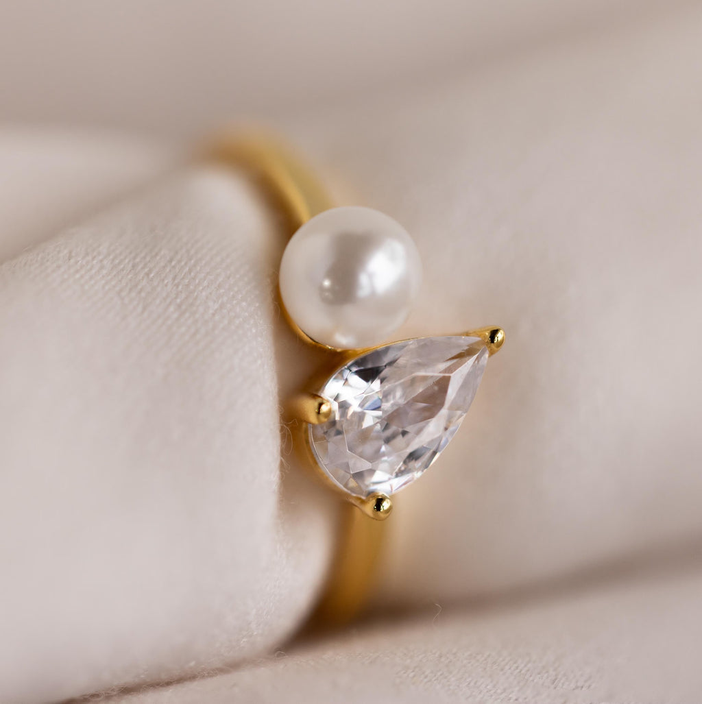 Close-up of the Pearl Diamond Ring on a soft fabric surface, emphasizing the glossy pearl and brilliant teardrop diamond.