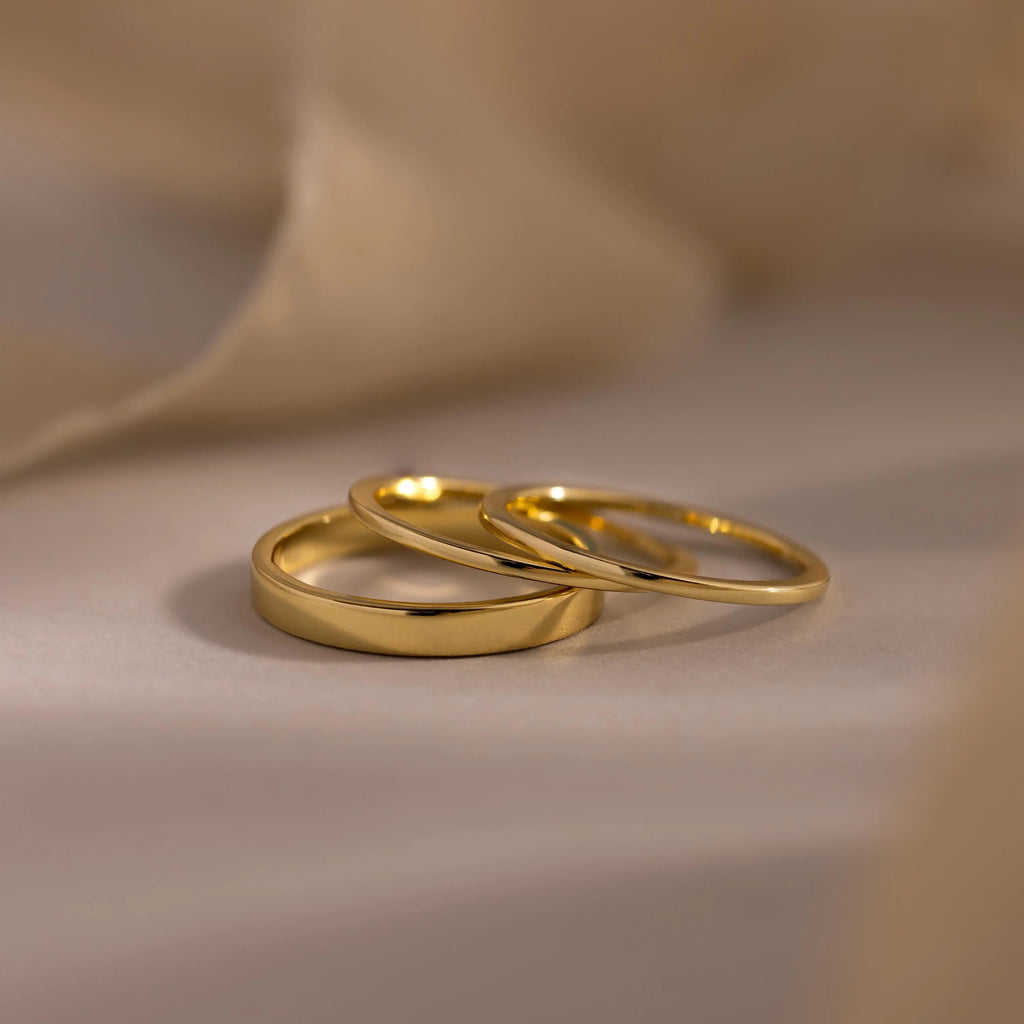 The Simple Ring Set features two minimalist gold rings placed together on a soft, light-colored surface with a blurred background.