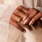 A hand with nude manicured nails wears the Peridot Baguette Signet Ring, resting on pleated cream fabric.
