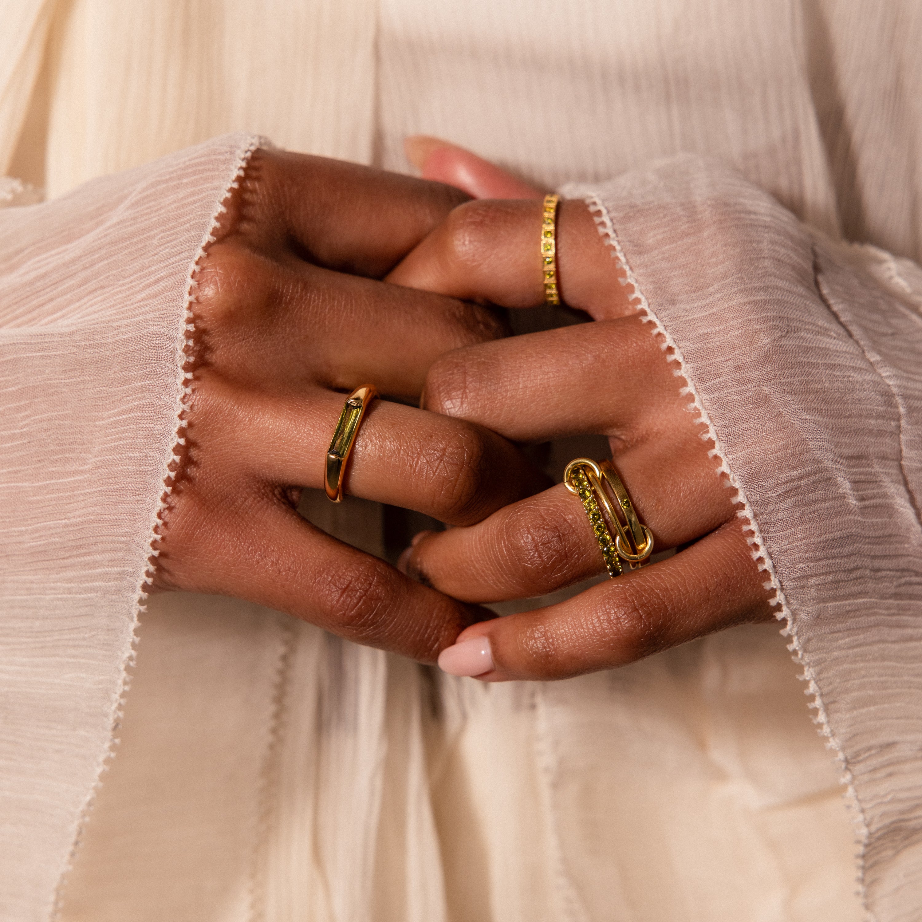 Close-up of hands with gold rings, including a modern statement ring and the Peridot Baguette Signet Ring, styled with a cream textured long-sleeve garment.