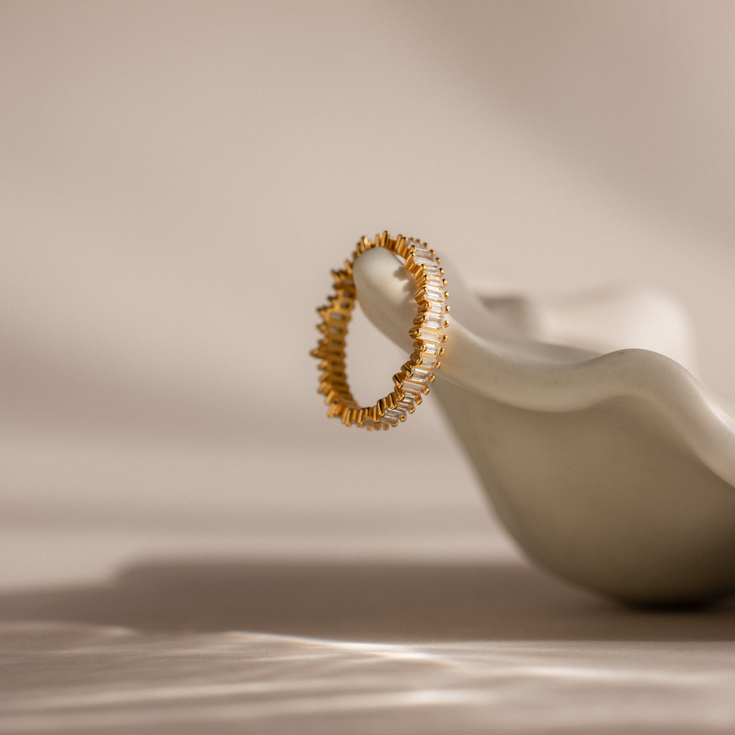 The Art Deco Rhythm Ring, featuring a textured gold design, rests on a smooth white sculptural surface under soft lighting.