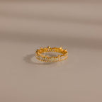 The Art Deco Rhythm Ring features rectangular baguette diamonds set in a continuous gold band, showcased on a smooth beige surface.