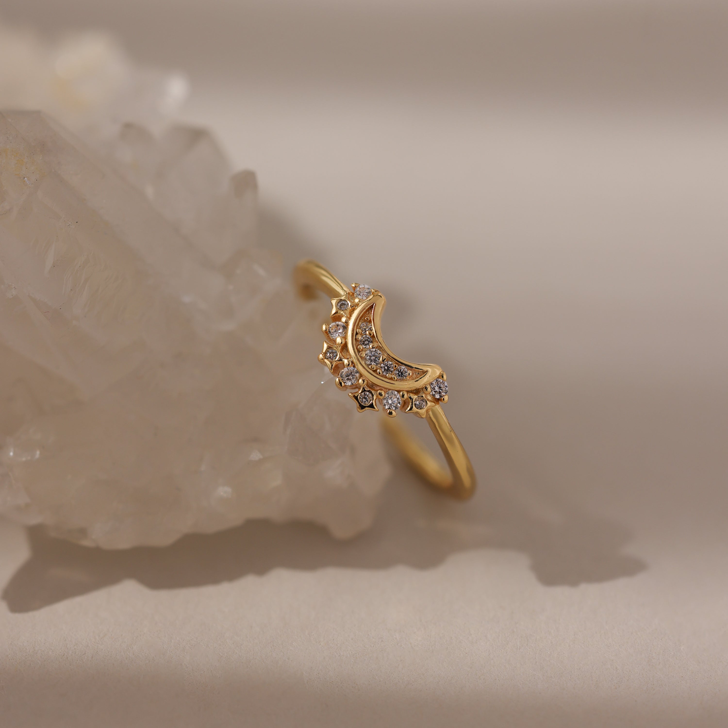 The Diamond Crescent Moon Ring, featuring a gold band with a crescent moon and small diamonds, is displayed on a clear crystal against a neutral background.
