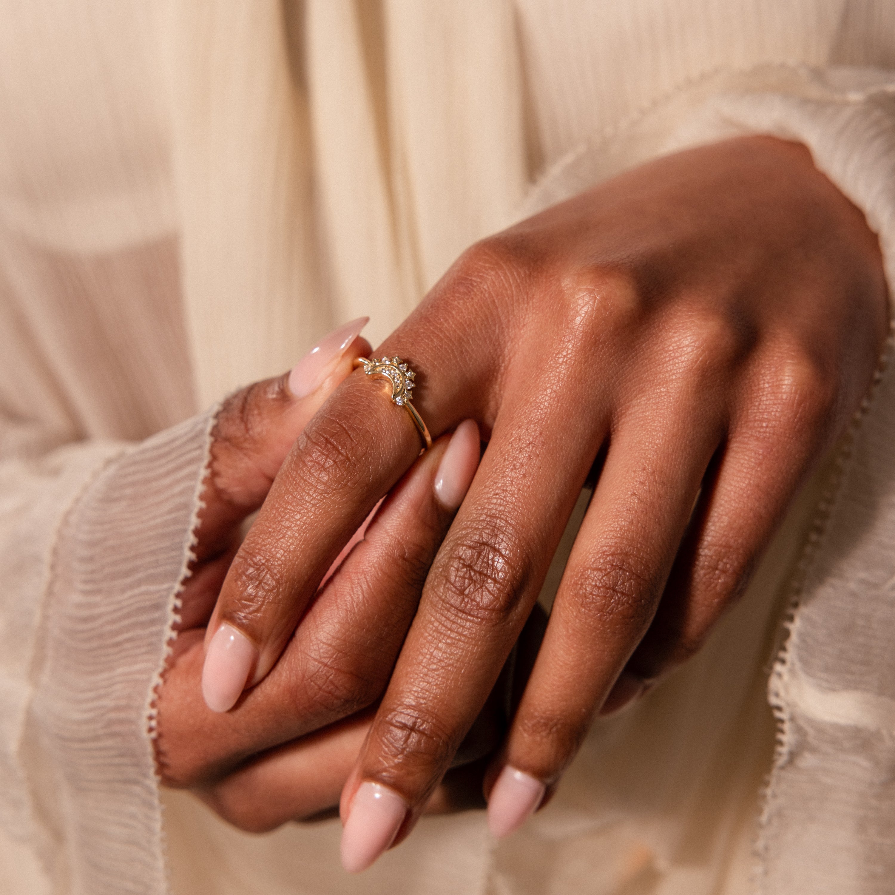 A close-up of hands with nude nails wearing the Diamond Crescent Moon Ring featuring a floral design.