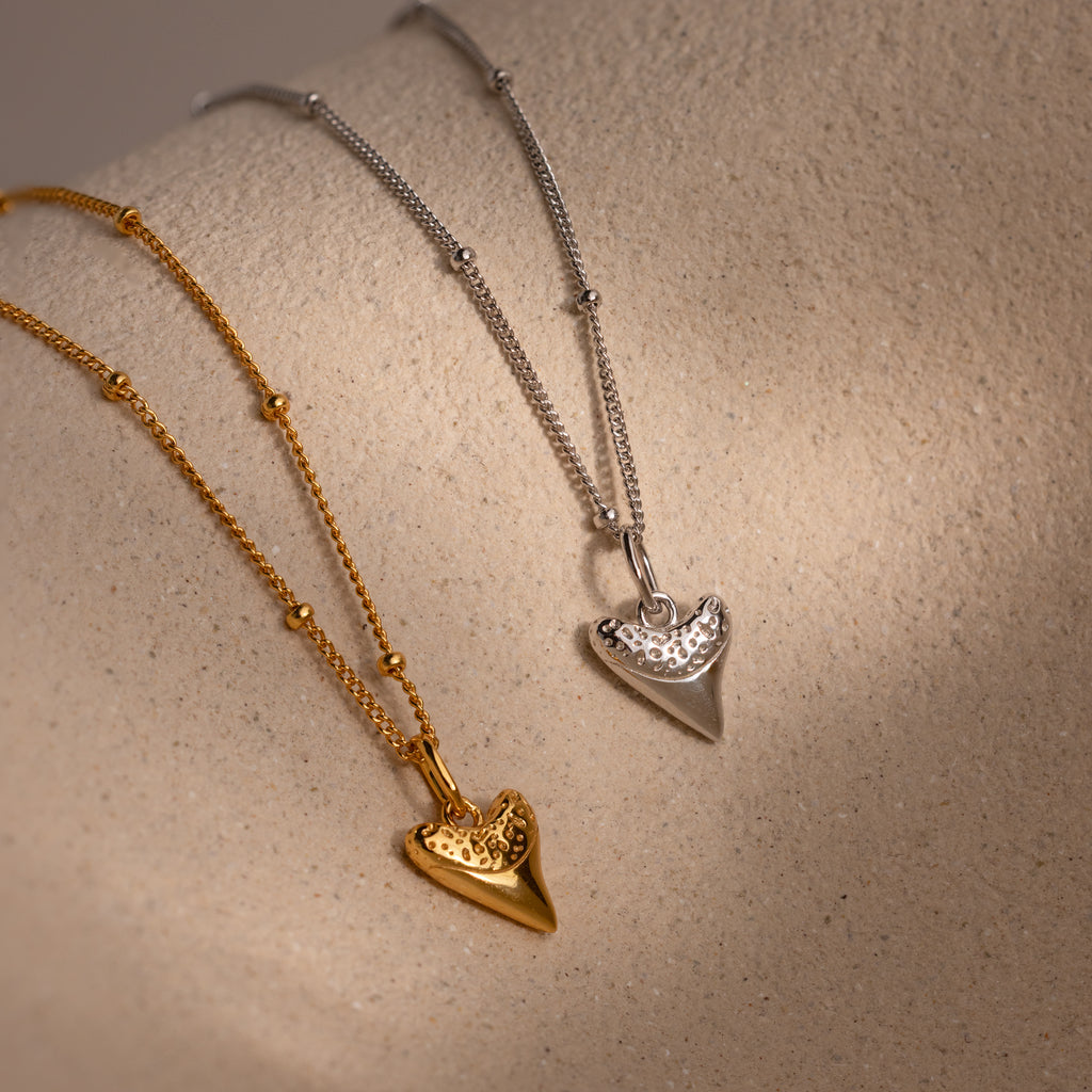 The Shark Tooth Necklace, available in both gold and silver finishes, brings a subtle beachside vibe—making it a standout in any coastal-inspired jewelry collection.