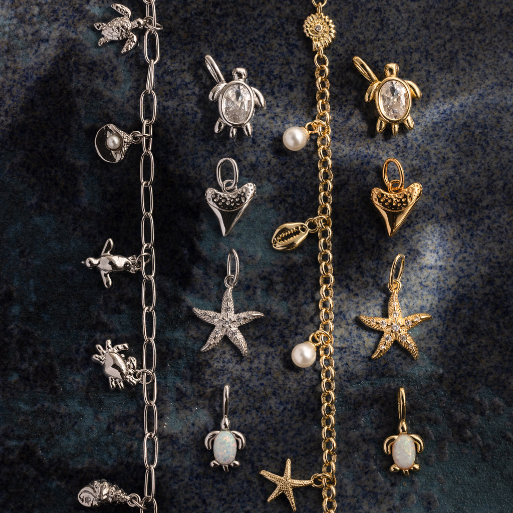 The Dainty Shark Tooth Charm in Silver features a sea-inspired design, perfect for coastal jewelry lovers, shown on a dark textured surface.