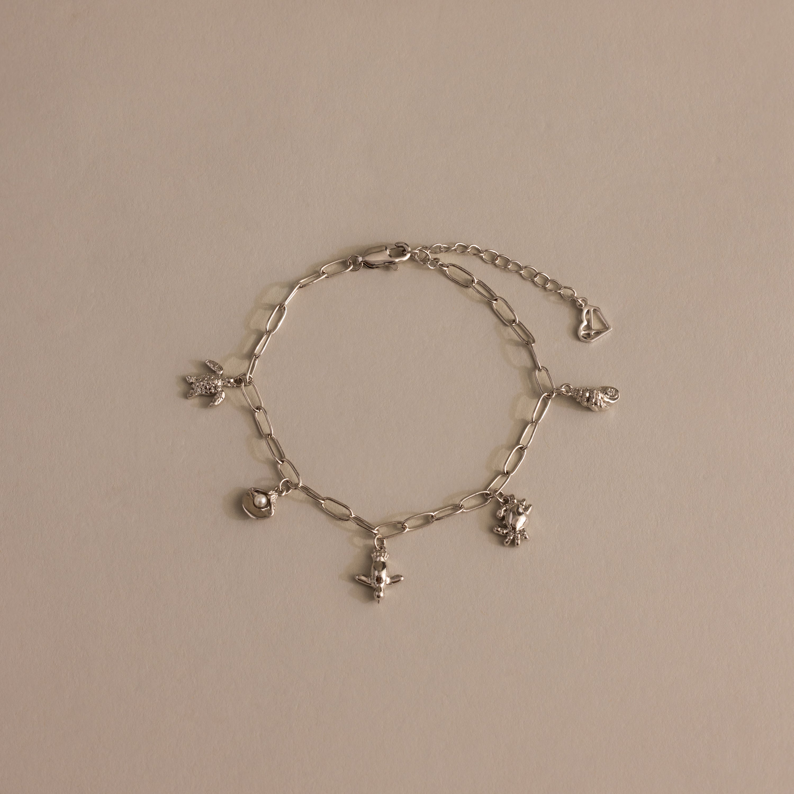 Seaside Charm Bracelet in Silver: Features five ocean-inspired charms—heart, angel, and animal—on a silver chain, displayed against a neutral beige background.