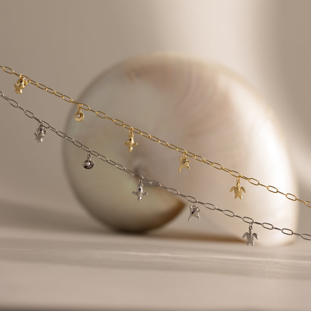 The Seaside Charm Necklace, displayed in front of a seashell on a neutral background, is perfect beach jewelry for adding a touch of coastal elegance.