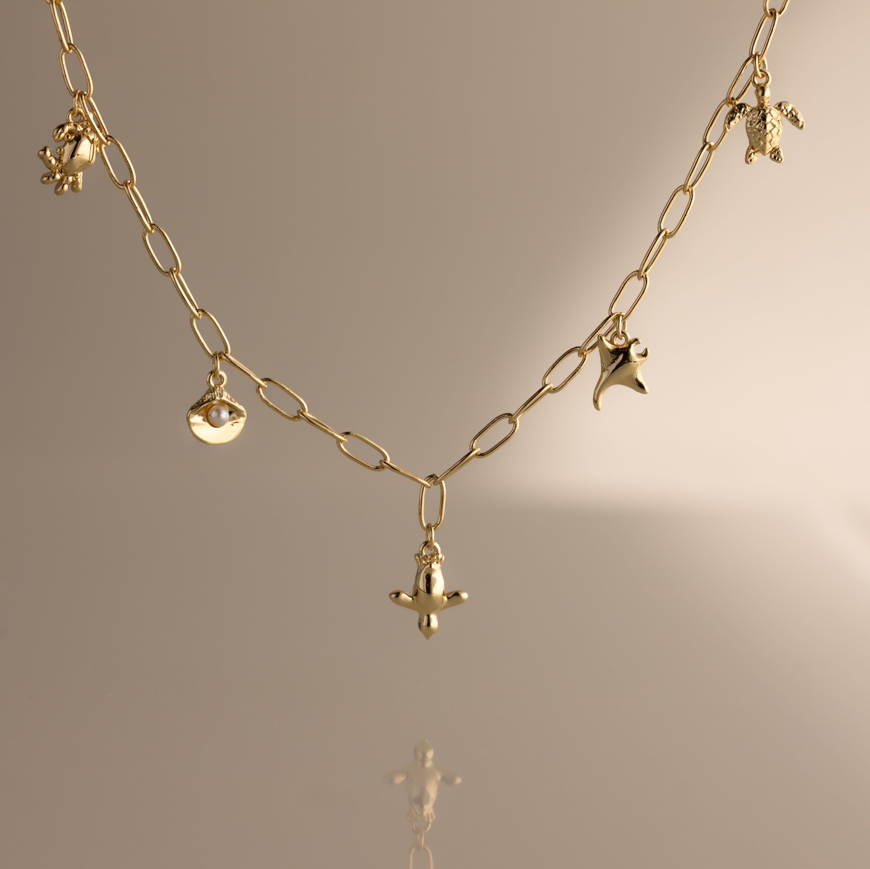Seaside Charm Necklace in 18K Gold: Delicate gold chain with small seaside charms, ideal as beach or summer jewelry, shown on a neutral beige background.