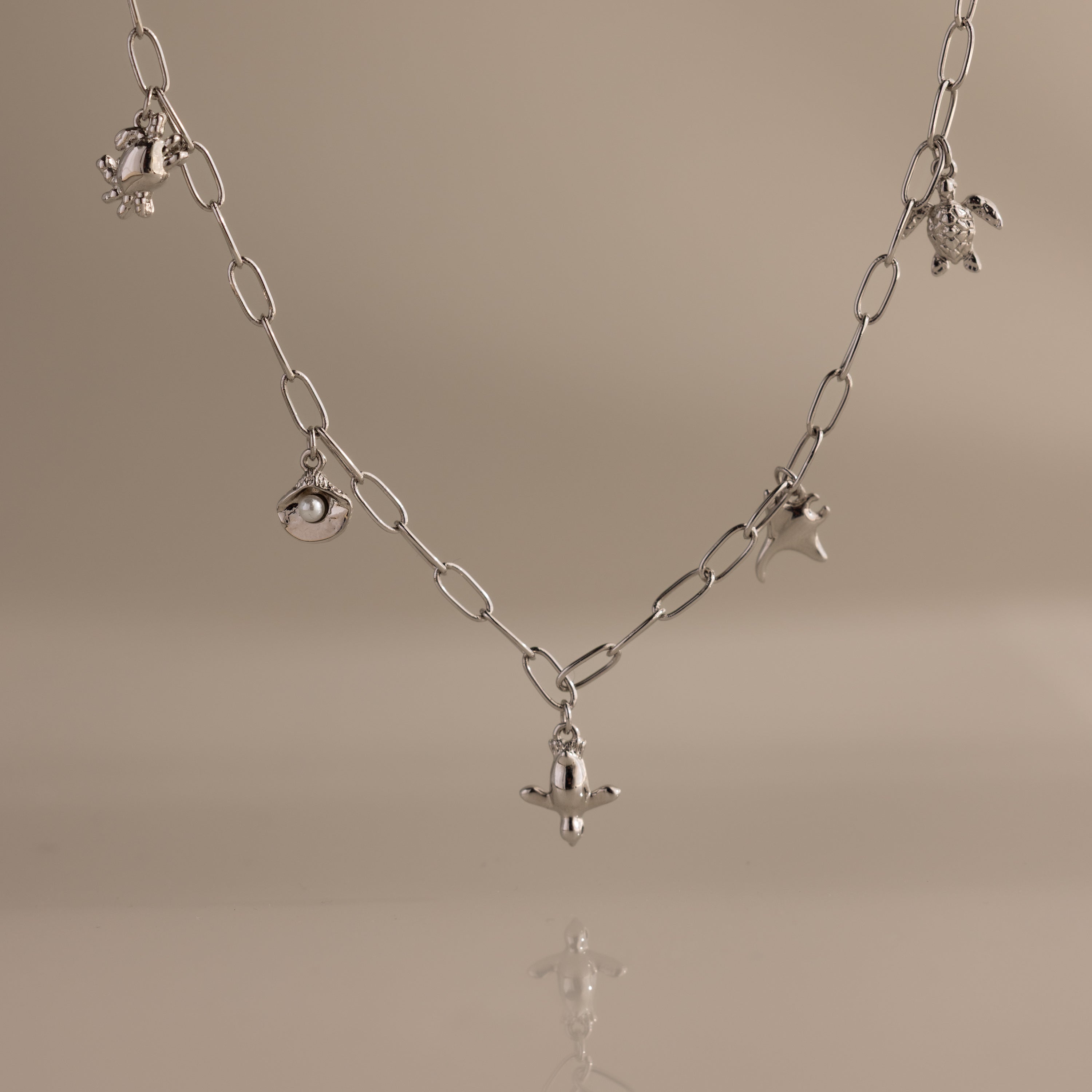 Seaside Charm Necklace in Silver featuring five ocean-themed charms on a plain beige background—perfect beach jewelry or summer accessory.