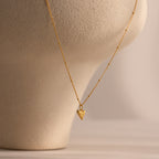 The Shark Tooth Necklace in 18K Gold, ideal for coastal jewelry lovers, is displayed on a textured beige mannequin bust against a neutral background.