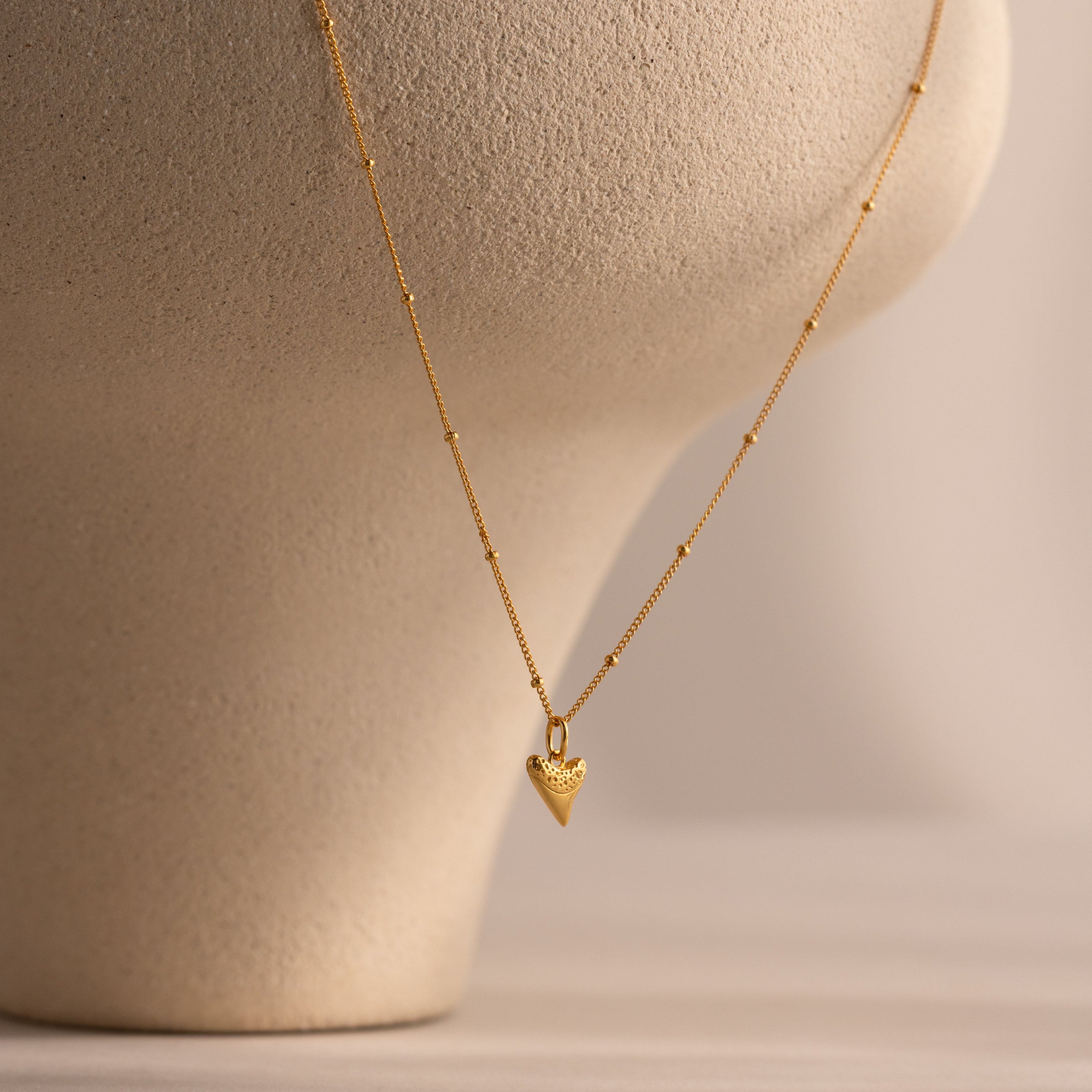 Shark Tooth Necklace displayed on a beige textured bust, perfect for adding coastal charm to your beachside look.