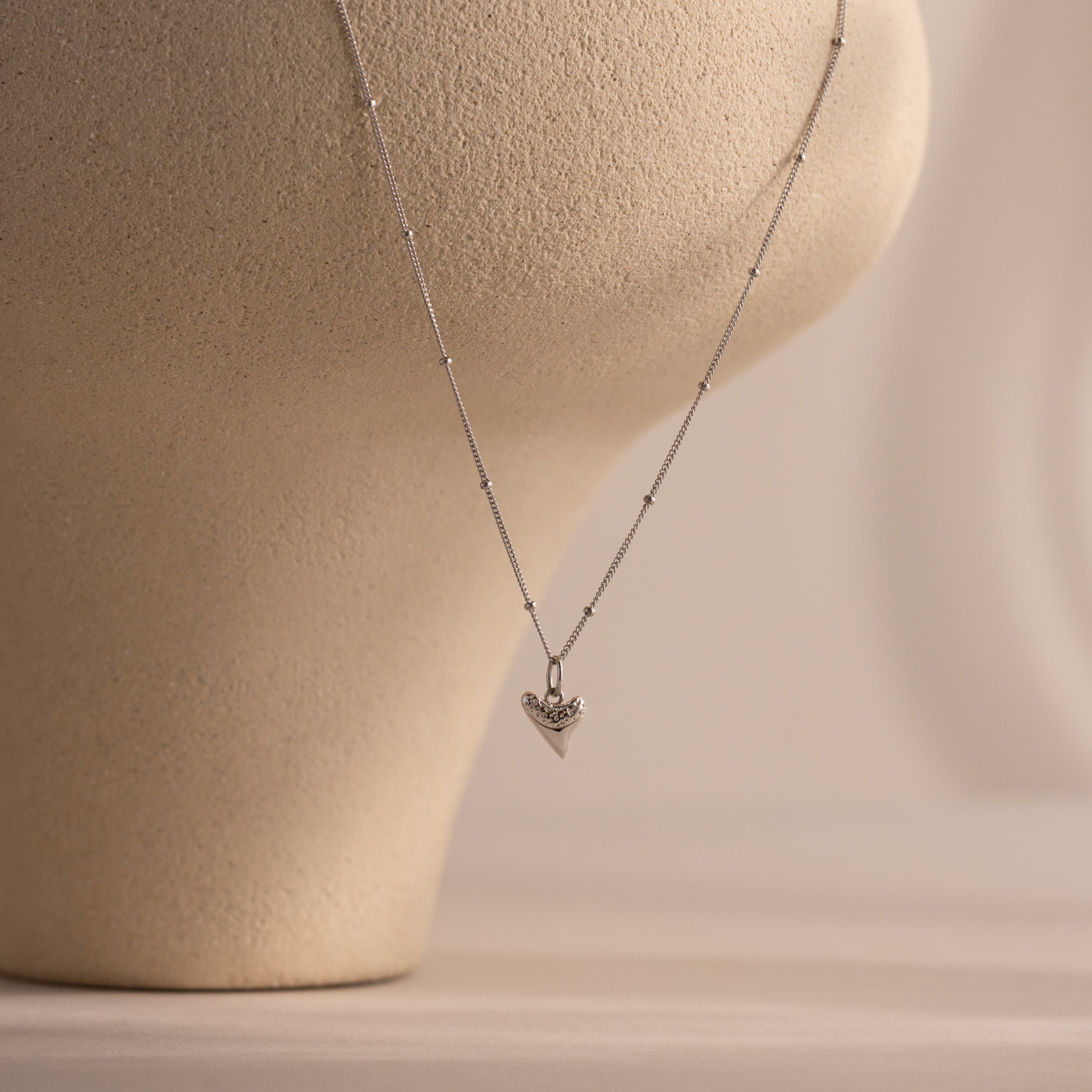 A silver Shark Tooth Necklace, perfect for a beachside aesthetic, displayed on a beige textured mannequin bust.