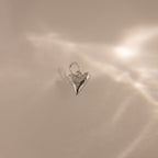 The Dainty Shark Tooth Charm in Silver shines on a neutral background with soft, diffused reflections—an elegant piece for any lover of coastal jewelry.