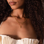 A woman shown from shoulders to lips wears a cream pleated strapless top and the Shark Tooth Necklace in 18K Gold, layered with other gold necklaces.