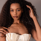 Woman with long curly hair wearing a cream pleated top and the Shark Tooth Necklace in 18K Gold, posing confidently.