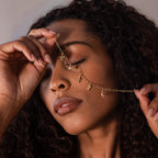 A woman with curly hair holds the Seaside Charm Bracelet in 18K Gold over her closed eyes, showcasing the beauty of this unique coastal-inspired jewelry piece.