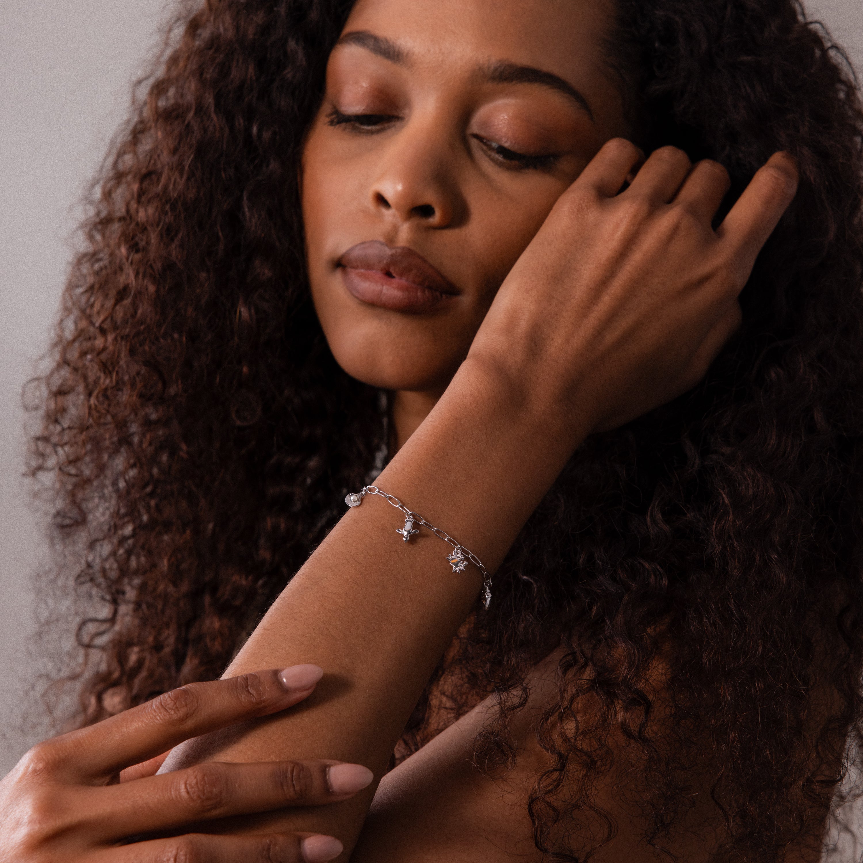A woman with curly hair poses with eyes closed, wearing the Seaside Charm Bracelet—an elegant accessory that adds a touch of coastal style to any outfit.