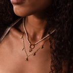 A woman wears layered gold and pearl necklaces featuring the Dainty Shark Tooth Charm; only her neck, chin, and curly hair show, evoking effortless coastal style.