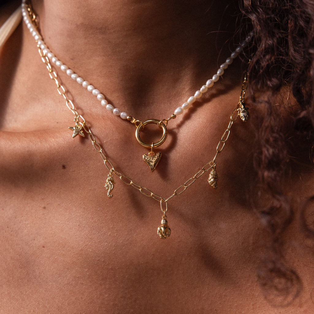 A person wearing layered gold necklaces and a pearl necklace featuring the Dainty Shark Tooth Charm, effortlessly showcasing coastal charm.