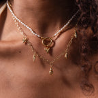 A person wearing layered gold necklaces and a pearl necklace featuring the Dainty Shark Tooth Charm, effortlessly showcasing coastal charm.