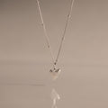 The Shark Tooth Necklace in Silver, displayed against a soft beige background, adds subtle coastal charm and beachside style to any look.