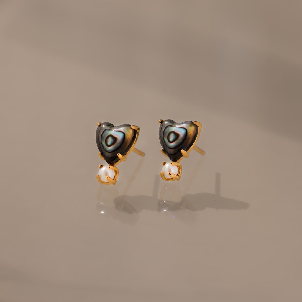 Abalone Pearl Heart Studs in 18K Gold feature heart-shaped abalone, gold accents, and dangling pearls—an elegant piece of coastal jewelry, beautifully displayed on a neutral background.