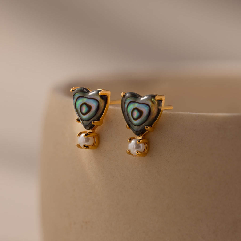 Abalone Pearl Heart Studs in 18K Gold featuring abalone inlay and delicate pearl accents, perfect coastal jewelry shown on a beige ceramic surface.