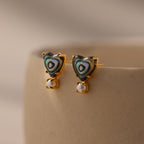 Abalone Pearl Heart Studs in 18K Gold featuring abalone inlay and delicate pearl accents, perfect coastal jewelry shown on a beige ceramic surface.