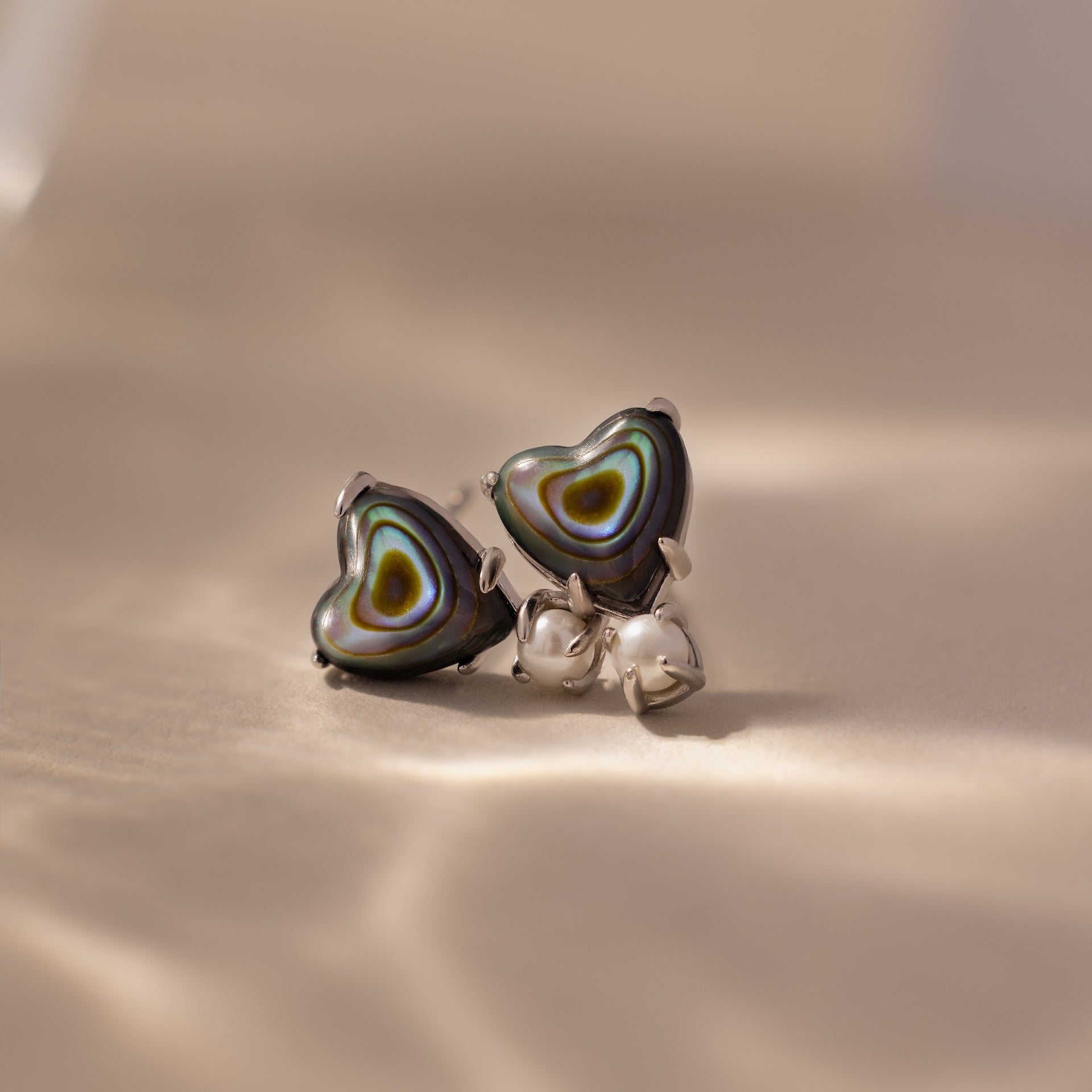 The Abalone Pearl Heart Studs feature heart-shaped abalone shell inlays, adding coastal charm to any look with their silver design and elegant shine.