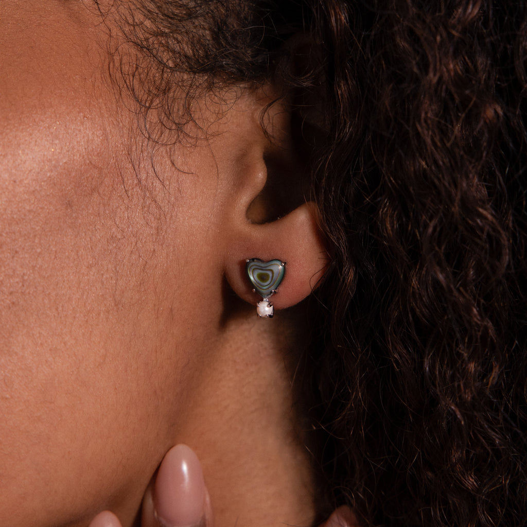 Close-up of a womans ear wearing Abalone Pearl Heart Studs in Silver—green abalone with a white gem, elegantly reminiscent of classic pearl earrings.