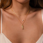A woman wears the Fish Pendant Necklace in Silver, featuring an ocean-inspired design with a fish pendant and small pearl, shown against bare skin and a cream top.